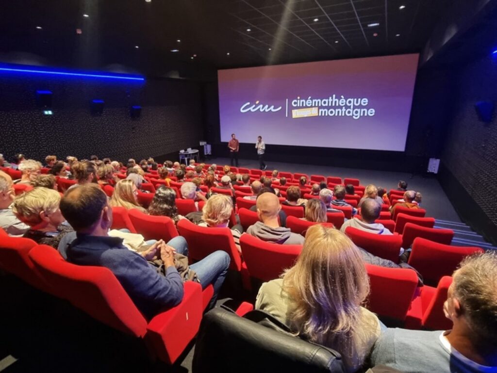 photo salle de cinema fauteuil rouge et gens de dos ecran au fond avec cinematheque de montagne