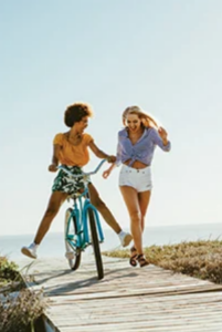 1 fille court à côté d'une autre qui est à vélo sur une allée en bois avec la mer derrière