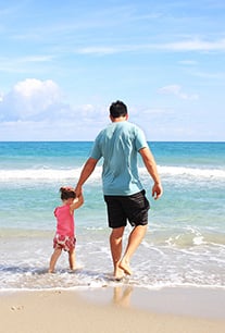 papa avec un enfant tenu par la main qui s'approche du bord de l'eau de la mer